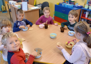 Dzieci siedzą przy stole i jedzą deserek owocowy