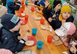 Dzieci z apetytem zajadają pachnącą kiełbaskę.